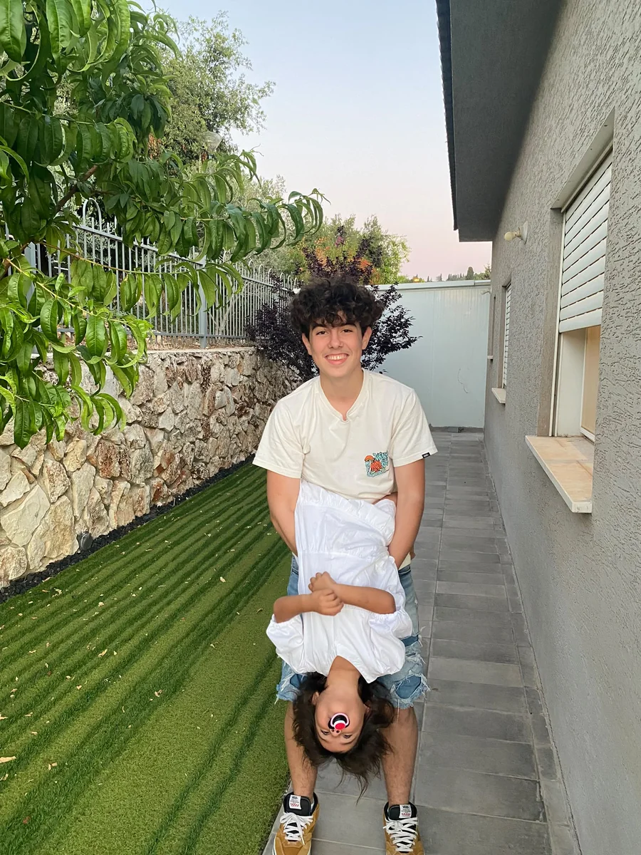 עומר מחייך בחצר ומחזיק ילדה קטנה הפוך